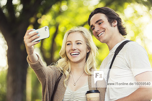 Ein junges Paar steht zusammen an einem Fahrradständer auf dem Universitätsgelände und nimmt mit einem Smartphone ein Selbstporträt auf; Edmonton  Alberta  Kanada