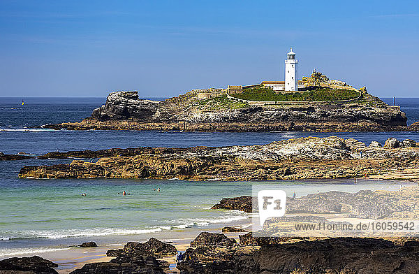White Godrevy Lighthouse on rock formation in blue water with blue sky and rocky shoreline  Godrevy Island in St. Ives Bay; Cornwall County  England
