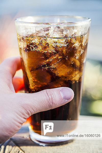 A hand holding a pint glass of cola with ice cubes; Long Beach  California  United States of America