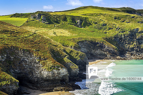 Felsige Klippen entlang der Küste mit grasbewachsenen Hügeln  blauem Himmel und Wolken; Grafschaft Cornwall  England