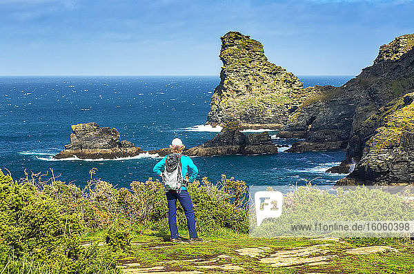 Weibliche Wanderin mit Blick auf Felsformationen und Klippen entlang der Küste mit blauem Himmel und Wolken; Cornwall County  England