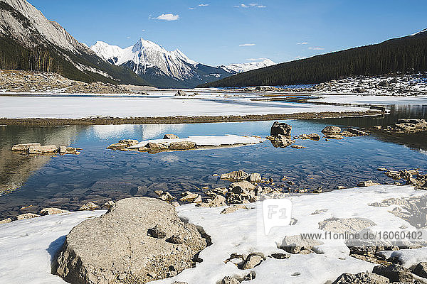 Snow on the lake and snow-capped rugged mountains peaks in Jasper National Park; Alberta  Canada