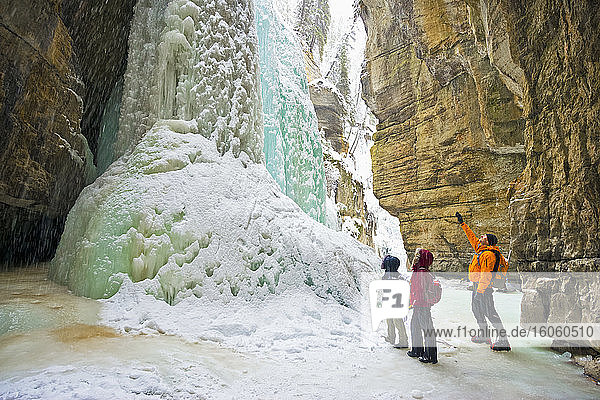 Drei Personen sehen einen großen gefrorenen Canyon-Wasserfall  Jasper National Park; Alberta  Kanada