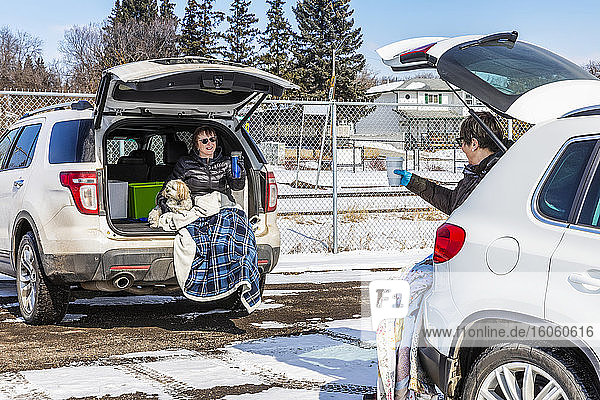 Two women sit in the back of their vehicles in a parking lot to visit during the Covid-19 world pandemic; St. Albert  Alberta  Canada