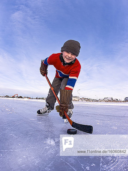 Junge Junge spielt Hockey im Freien auf einer gefrorenen Eisbahn; Alberta  Kanada