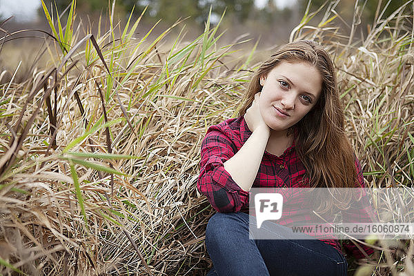 Porträt eines Mädchens  das auf einem Feld aus hohem Gras sitzt und in die Kamera schaut; Toronto  Ontario  Kanada