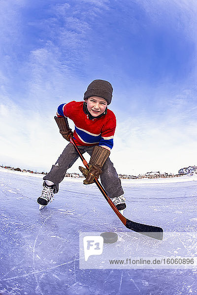 Young boy playing hockey outdoors on a frozen rink; Alberta  Canada