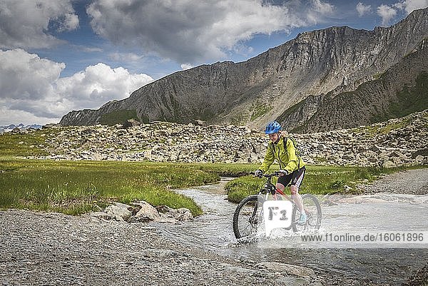 Mountainbikerin fährt auf alpiner Schotterstraße durch Bergfluss  Serfaus  Tirol  Österreich  Europa