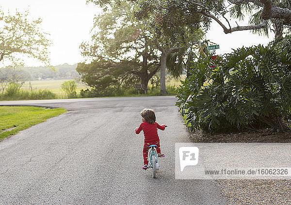 Ein fünfjähriger Junge im roten Hemd mit dem Fahrrad in einer ruhigen Wohnstraße.