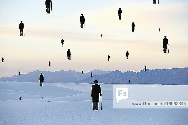 Men in bowler hats with umbrellas outline of figures floating above ground in a sand dune desert
