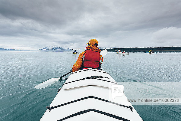 Eine Person  die in einem Doppel-Seekajak auf ruhigem Wasser vor der Küste Alaskas paddelt.