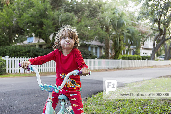 A five year old boy in a red shirt riding his bike on a quiet residential street.