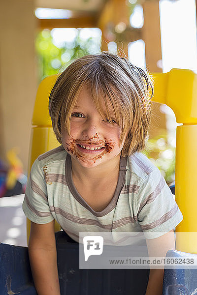 Porträt eines lächelnden 4-jährigen Jungen mit Schokolade im Gesicht  der mit der älteren Schwester spielt