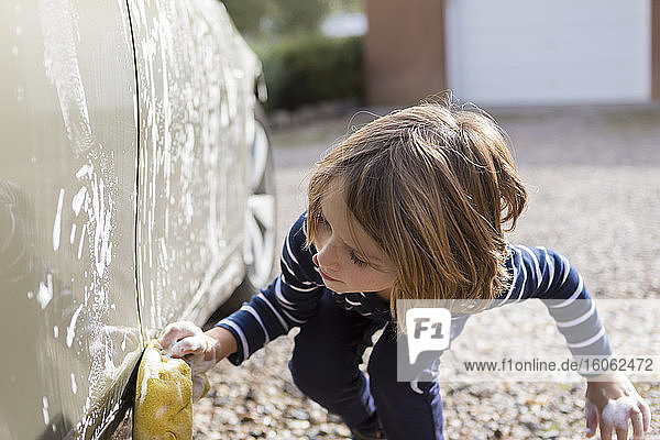4 Jahre alter Junge  der auf dem Parkplatz ein Auto wäscht