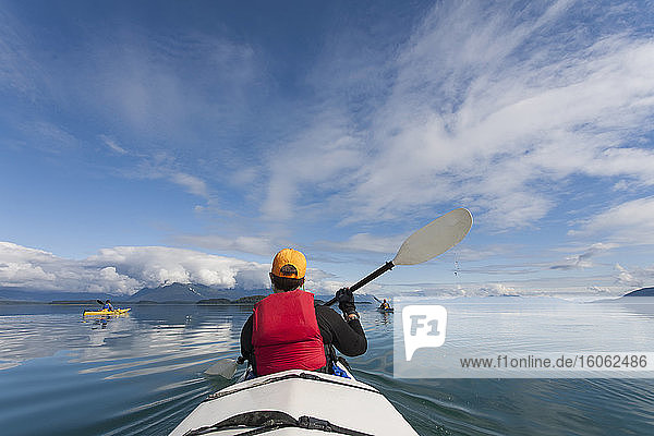A small group of people kayaks in pristine waters of an inlet on the Alaska coastline.