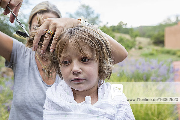 5 Jahre alter Junge lässt sich draußen von der Mutter die Haare schneiden