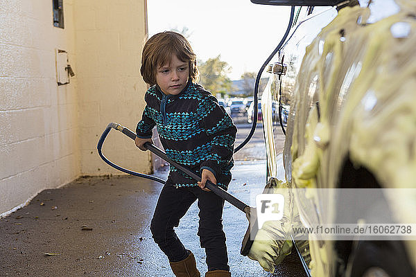 4 Jahre alter Junge  der in einer Autowaschanlage ein Auto wäscht