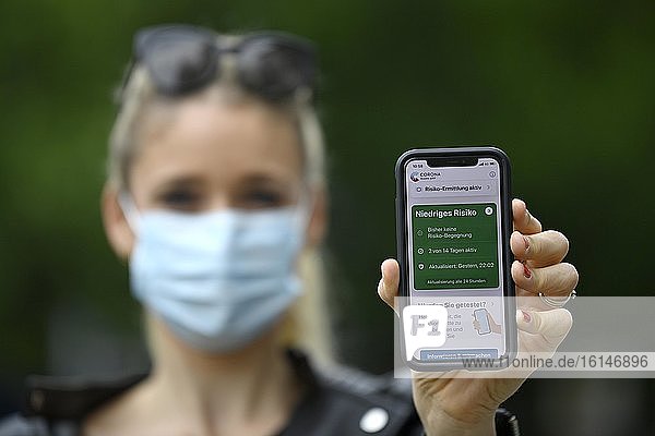 Frau mit Mundschutzmaske zeigt Smartphone mit Corona Warn-APP  niedriges Risiko  Corona-Krise  Baden-Württemberg  Deutschland  Europa