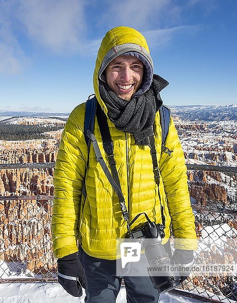 Portrait  young man in winter clothes with camera at the viewpoint  rocky landscape with hoodoos in winter  Rim Trail  Bryce Canyon National Park  Utah  USA  North America