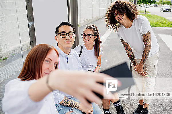 Mixed race group of friends hanging out together in town  taking selfie with mobile phone.