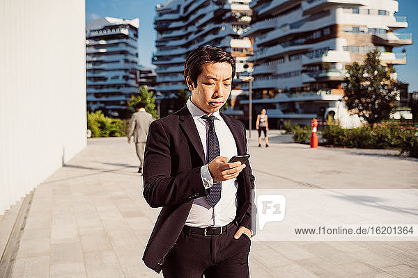 Porträt eines asiatischen Geschäftsmannes in dunklem Anzug  der sein Mobiltelefon überprüft.