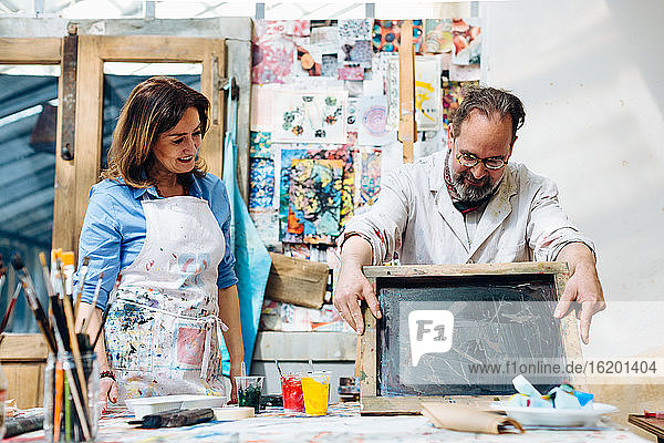 Frau beobachtet Mann bei Siebdruckarbeiten im Kreativstudio