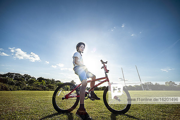 Porträt eines Jungen  der auf seinem BMX-Fahrrad sitzt und einen Fahrradhelm trägt.