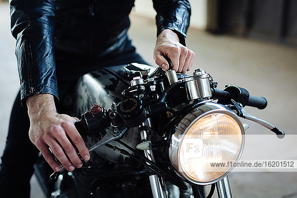 Young male motorcyclist straddling vintage motorcycle in garage  cropped