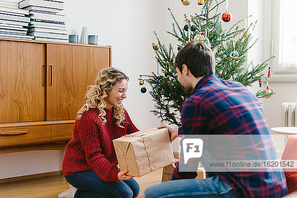 Couple placing gifts under Christmas tree at home