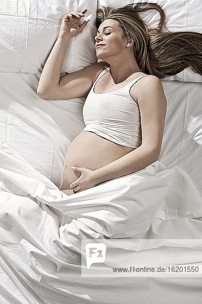 Porträt einer hochschwangeren Frau auf dem Bett liegend  den Bauch wiegend.