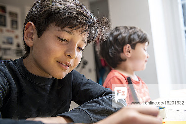 Two boys with brown hair sitting at table  doing homework.