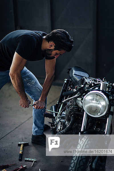 Young male motorcyclist repairing vintage motorcycle in garage