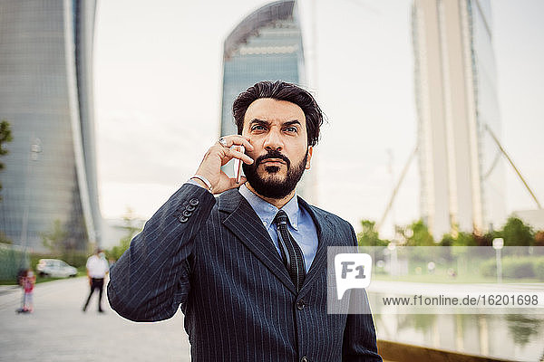 Porträt eines bärtigen Geschäftsmannes in dunklem Anzug  der ein Mobiltelefon benutzt.