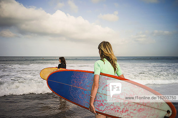 Zwei Frauen  die mit ihren Surfbrettern aufs Meer hinausgehen  Seminyak  Bali  Indonesien