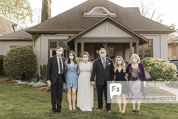Hochzeitsgesellschaft posiert für ein Gruppenporträt auf dem Vorgarten und trägt während der Coronavirus-Krise Gesichtsmasken.