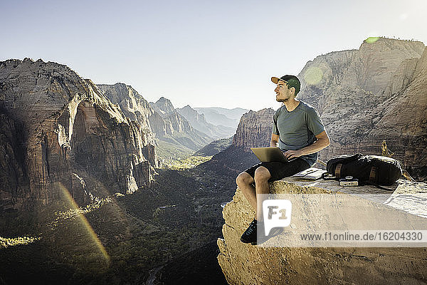 Mann wandert auf dem Angels Landing Trail  sitzt auf einem Felsen und benutzt einen Laptop  Zion National Park  Utah  USA