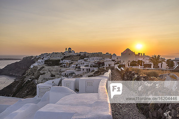 Blick auf weiß getünchte Mauern und die Stadt bei Sonnenuntergang  Oia  Santorin  Griechenland