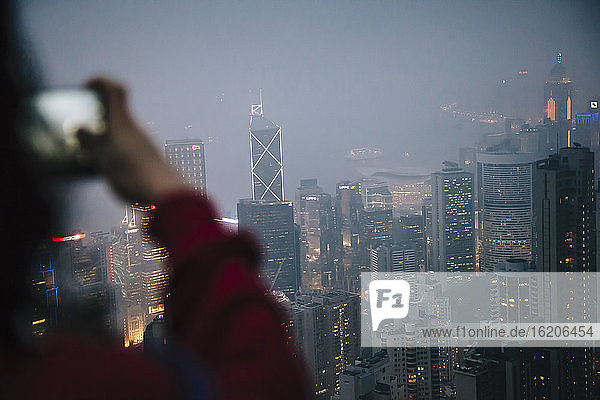 Blick über die Schulter eines Touristen,  der vom Victoria Peak aus Wolkenkratzer bei Nacht fotografiert,  Hongkong,  China