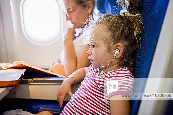 junges Mädchen mit Kopfhörern im Flugzeug