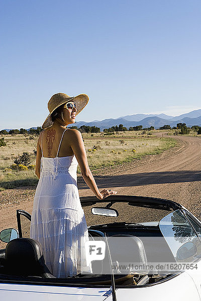 Native American woman in sun dress driving a white convertible sports car on desert dirt road