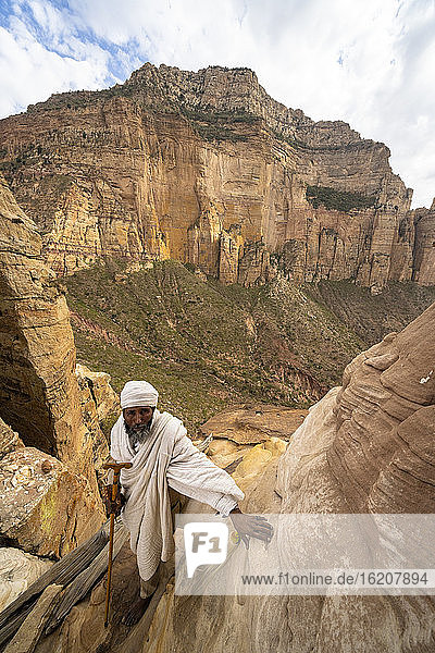 Äthiopischer Priester  der sich an steile Felsen lehnt  die zur Kirche Abuna Yemata Guh führen  Gheralta-Gebirge  Region Tigray  Äthiopien  Afrika