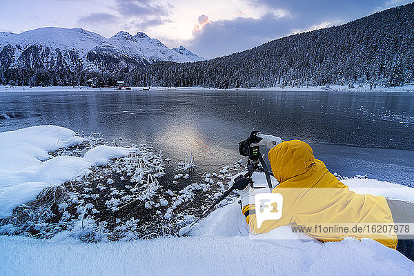 Fotograf beim Fotografieren des gefrorenen Lej da Staz in der Morgendämmerung auf dem Schnee liegend  Engadin  Kanton Graubünden  Schweiz  Europa