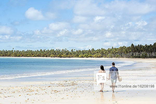 A good-looking Hispanic (Latin) couple walking on a deserted beach with backs to camera  Brazil  South America