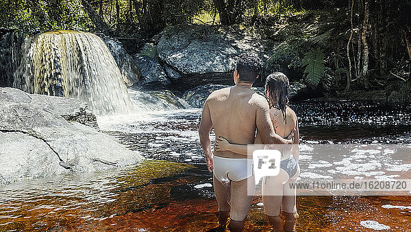 Ein junges  heterosexuelles  verliebtes lateinamerikanisches Paar genießt einen unberührten Gebirgsbach im brasilianischen Regenwald  Minas Gerais  Brasilien  Südamerika