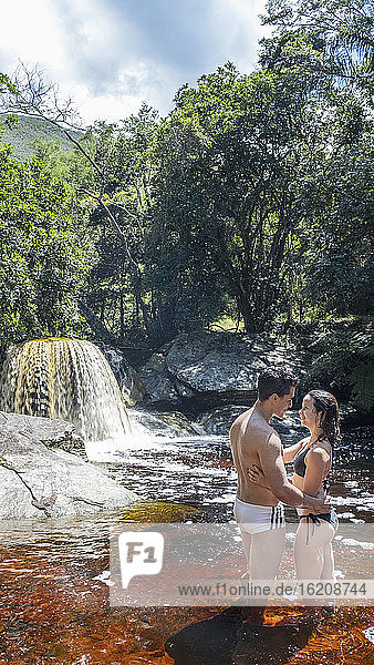 Ein junges heterosexuelles verliebtes lateinamerikanisches Paar genießt ein Bad in einem Gebirgsbach im unberührten Regenwald  Minas Gerais  Brasilien  Südamerika