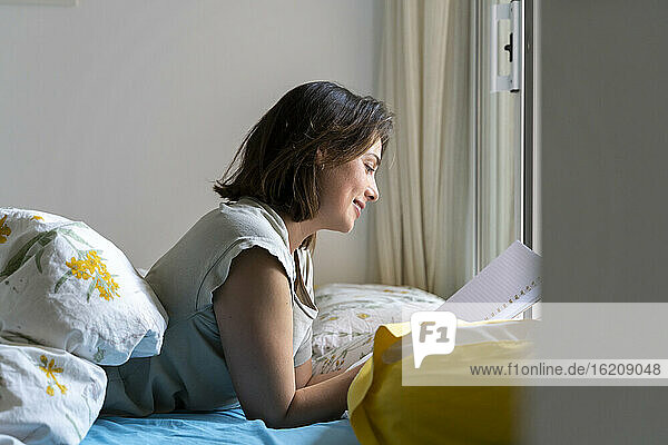 Lächelnde Frau  die im Schlafzimmer auf einem Notizblock liest