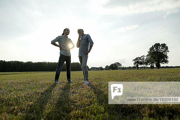 Father and adult son standing on a meadow in the countryside at sunset