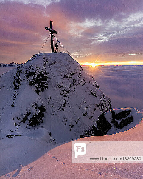 Silhouette einer Frau  die den stimmungsvollen Sonnenuntergang am Kreuz auf dem Gipfel des Aggensteins bewundert