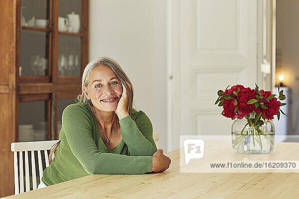 Lächelnde Frau träumt am Tisch zu Hause