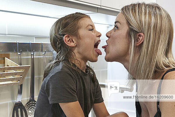 Nahaufnahme von fröhlicher Mutter und Tochter  die sich in der Küche gegenseitig Zungen zeigen